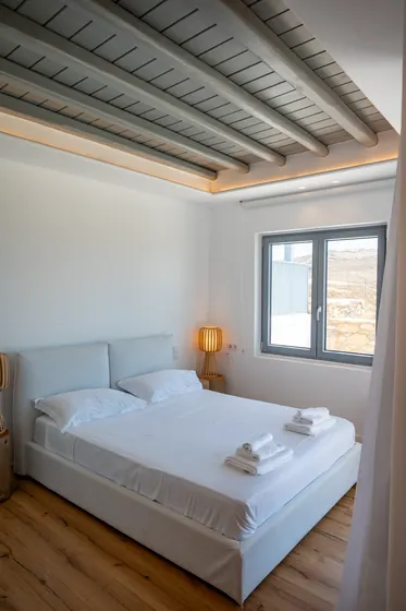 Bright minimalist bedroom with exposed beams and warm ambient lighting