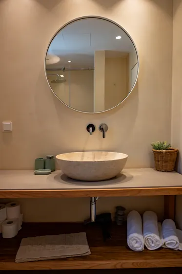 Spa-inspired bathroom with stone sink, round mirror, and open shelving